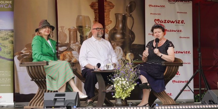 Dwie kobiety i mężczyzna siedzący przy stoliku na scenie.