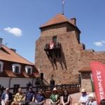 10 osób siedzących w półkolu. W tle wieża Zamku w Liwie.