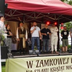 Osoby na scenie, jedna przemawia trzymając mikrofon.