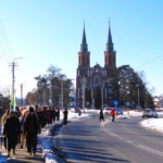 Tłom ludzi idących gęsięgo. Zimowa sceneria. W tle dwie wieże liwskiego kościoła.