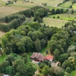 Zdjęcie z drona Dworu w Paplinie. Budynek otoczony zielenią - ogrodem i drzewami.