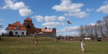 Dziecko puszczające latawiec. W tle przechodzący ludzie i Zamek w Liwie.