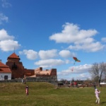 Dziecko puszczające latawiec. W tle przechodzący ludzi i Zamek w Liwie.