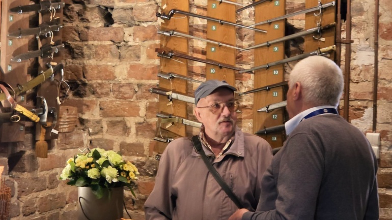 Dwaj mężczyźni, jednym jest darczyńca, w tle na ceglanej ścianie powieszone bagnety