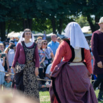 Uczestnicy w strojach historycznych tańczą na festiwalu, a w tle widać licznie zgromadzoną publiczność
