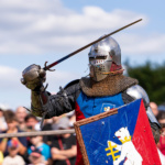Rycerz w stalowym hełmie, z tarczą i mieczem, staje do walki przed widownią podczas festiwalu historycznego