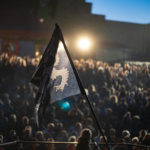 Na tle tłumu ludzi jeden z uczestników trzyma flagę z wizerunkiem gryfa, oświetloną przez reflektory