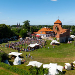 Na tle zamku, w otoczeniu zieleni, odbywa się festiwal z liczną grupą uczestników oraz stoiskami z namiotami