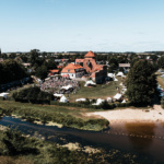 Widok na festiwal odbywający się przy średniowiecznym zamku, z rozstawionymi namiotami, tłumem ludzi i rzeką w tle