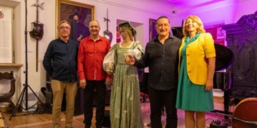 Czterech mężczyzn i kobieta pozują obok manekina w historycznym stroju, w pomieszczeniu z dekoracjami i instrumentami muzycznymi